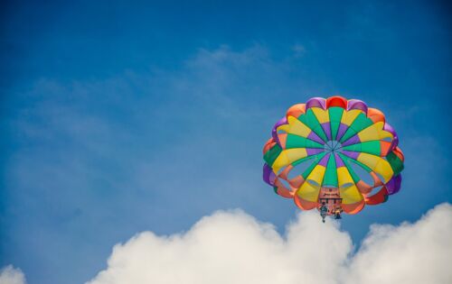 Von unten gegen den blauen Himmel aufgenommen: ein bunter, geöffneter Fallschirm, der zwei Personen trägt.